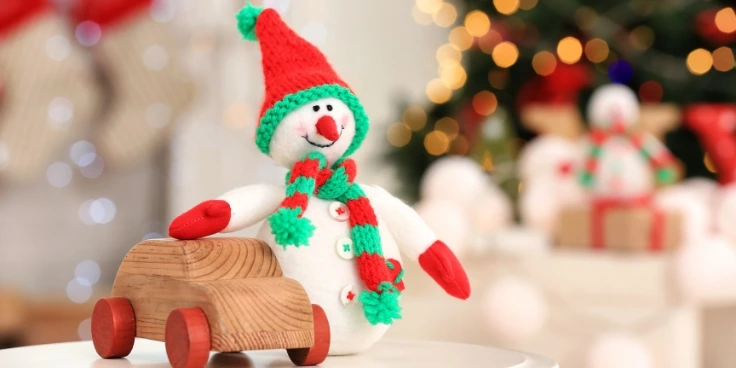 Selbstgebastelter schneemann mit mütze neben holzauto vor weihnachtsbaum