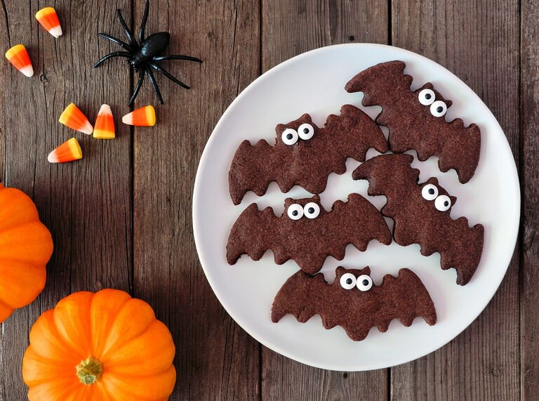 Teller mit lustigen fledermausförmigen Halloween-Keksen mit Zuckeraugen, umgeben von Kürbissen