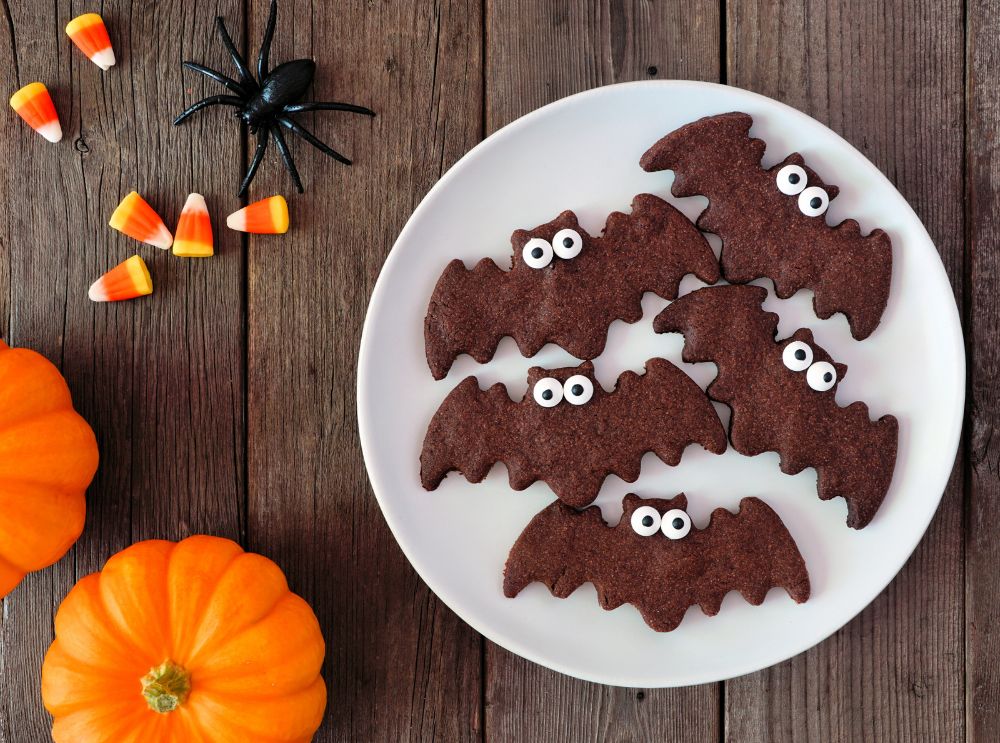 Teller mit lustigen fledermausförmigen Halloween-Keksen mit Zuckeraugen, umgeben von Kürbissen