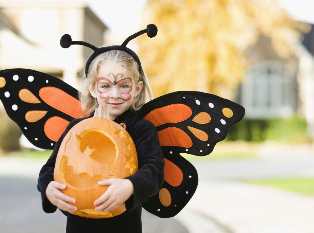 Halloween mit kindern – kreative kostüme, bastelideen und kinderfreundliche snacks 3 Kind im schmetterlings-kostüm hält einen geschnitzten kürbis