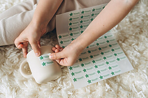 Kinderhände kleben einen personalisierten Namensaufkleber mit dem Text "Noah" auf eine Tasse