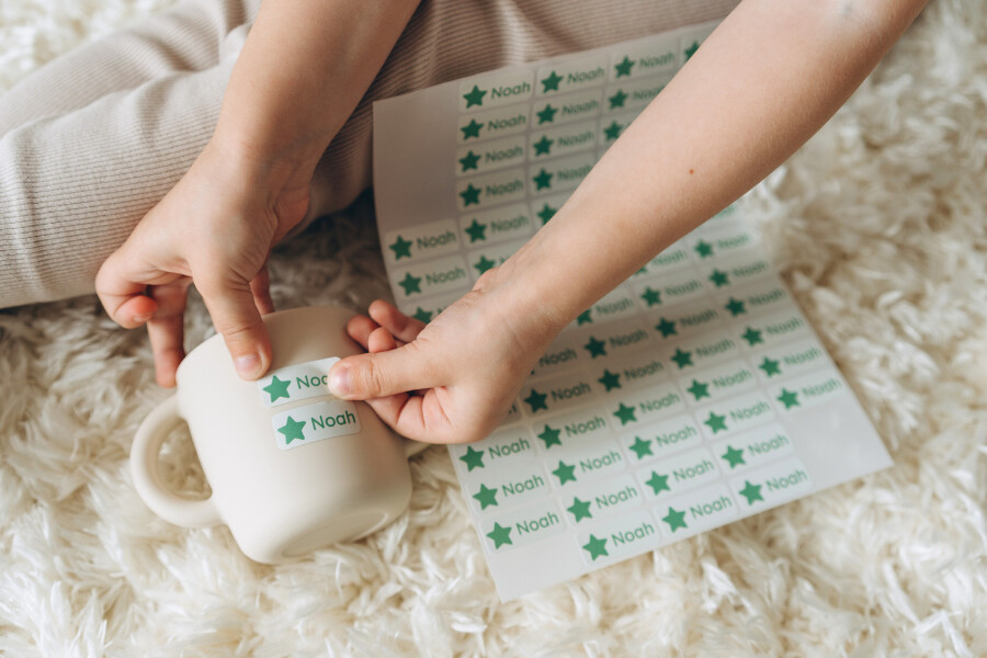 Kreative montessori‑bastelideen: so fördern kleine hände die fantasie 8 Kinderhände kleben einen personalisierten namensaufkleber mit dem text "noah" auf eine tasse