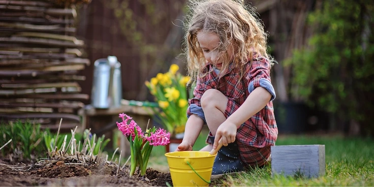 Kind pflanzt eine Pflanze im Garten ein und spielt.