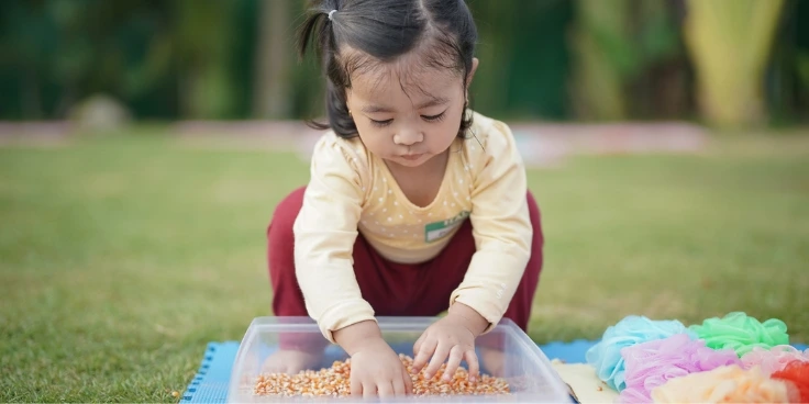 Kleinkind spielt mit maiskörnern in einer kleinen wanne.
