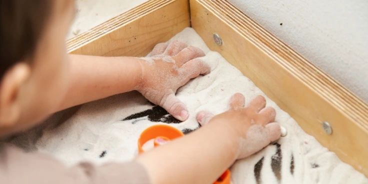 Montessori für vorschulkinder: so lernen sie mathe und sprache mit spaß 4 Kind schreibt zahlen in einer montessori-sandwanne.