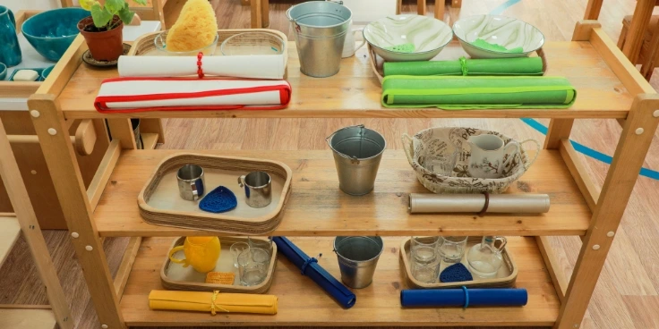 Montessori-regal mit sortierten alltagsmaterialien und tabletts für praktisches leben