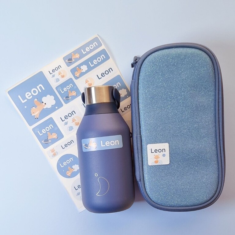 Blaue Trinkflasche und Mäppchen mit personalisierten Namensaufklebern neben einem passenden Set mit Fuchs-Aufklebern mit dem Text "Leon"