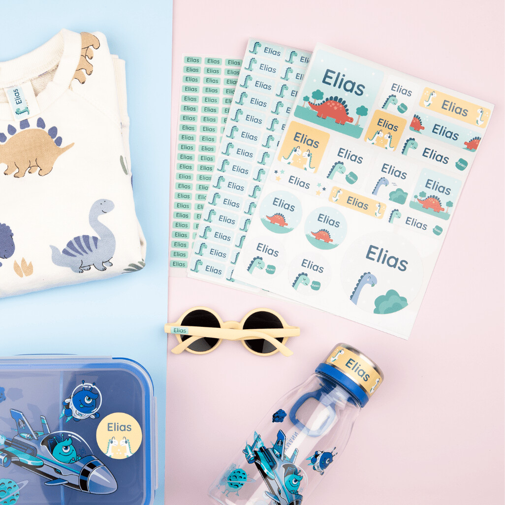 Wann sind große namensaufkleber die bessere wahl? Einsatzbereiche und tipps 2 Ein set mit großen namensaufklebern mit dem text "elias" und einem dinosaurier-design, zusammen mit passenden personalisierten accessoires und weiteren aufkleber-sets in verschiedenen größen