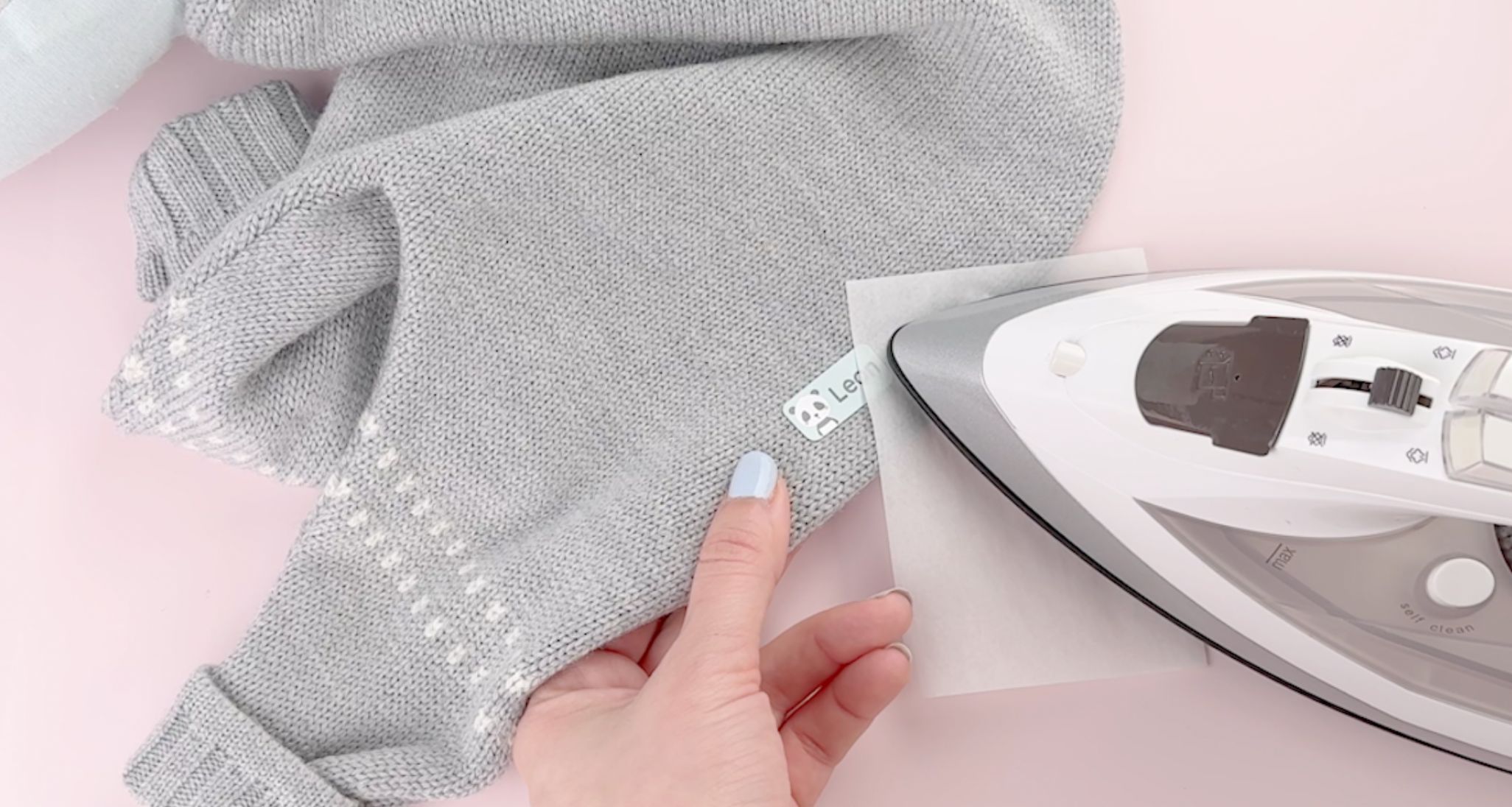 Wie kann man bügeletiketten wieder entfernen? Schritt-für-schritt-anleitung 3 Bügeletikett mit dem namen leon wird auf ein graues gestricktes babykleidungsstück aufgebügelt