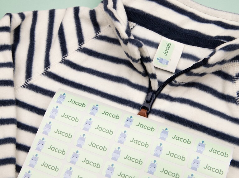 Bogen mit grünen Namensaufklebern mit Nilpferdmotiv, ein Aufkleber platziert auf einem gestreiften Kinder-Shirt