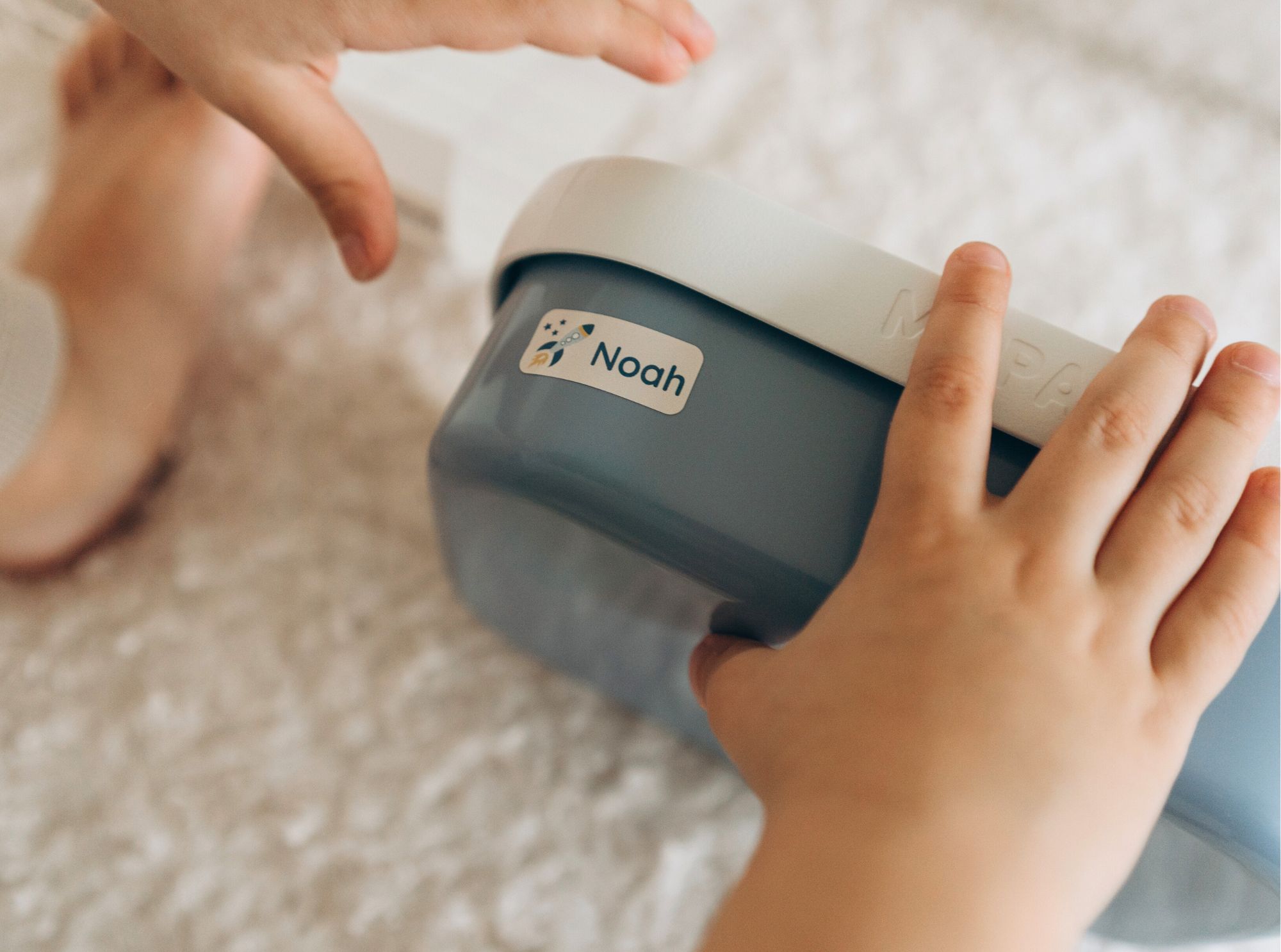 Kinderhände halten eine blaue brotdose mit einem personalisierten namensaufkleber mit dem namen noah