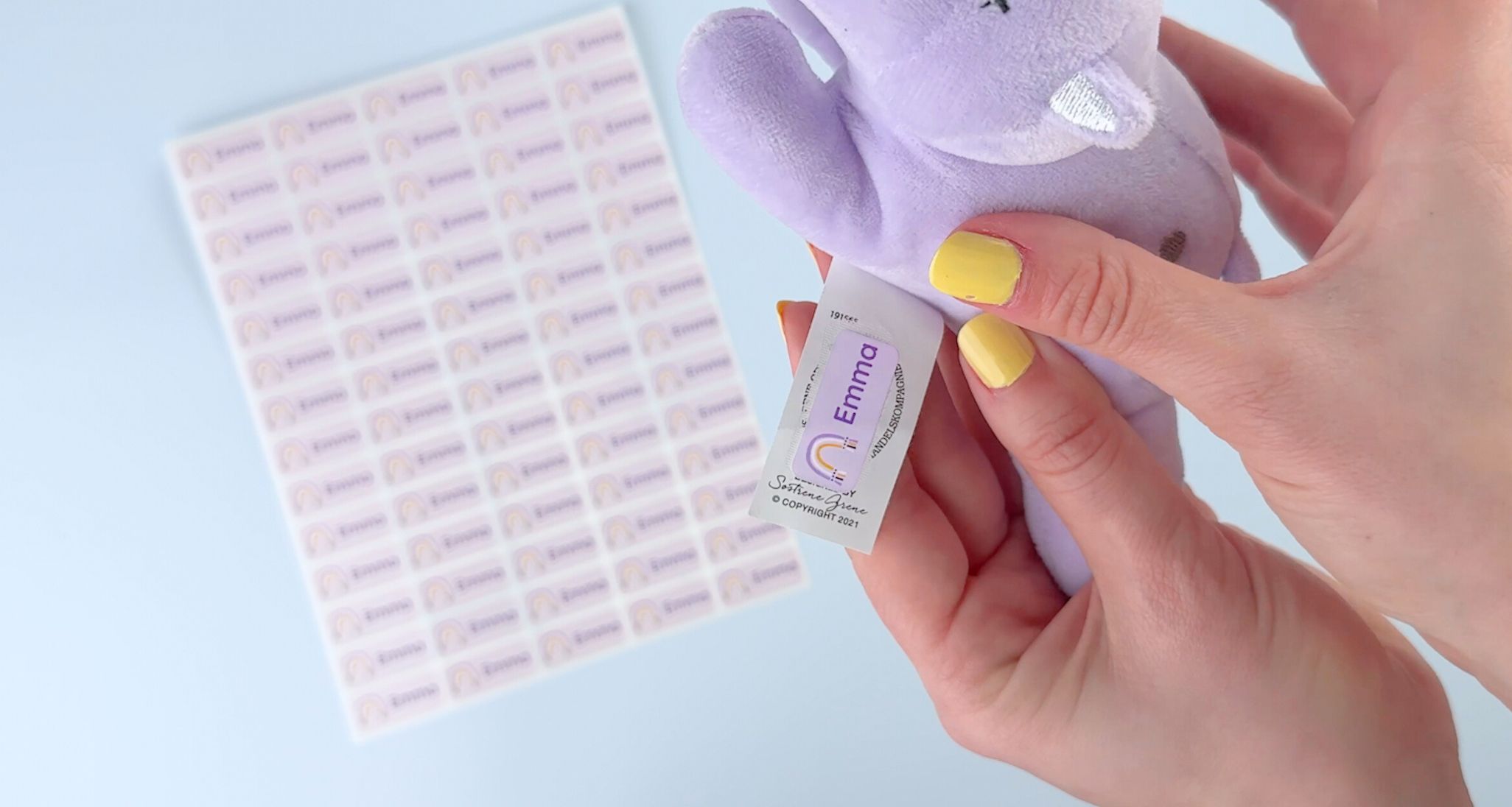 Anbringung eines rosa namensaufklebers mit dem namen emma auf einem etikett eines lila kuscheltiers