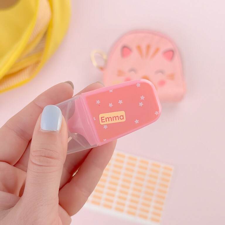 Hand hält einen rosa Marker mit dem Namen Emma, im Hintergrund weitere Mini-Namensaufkleber