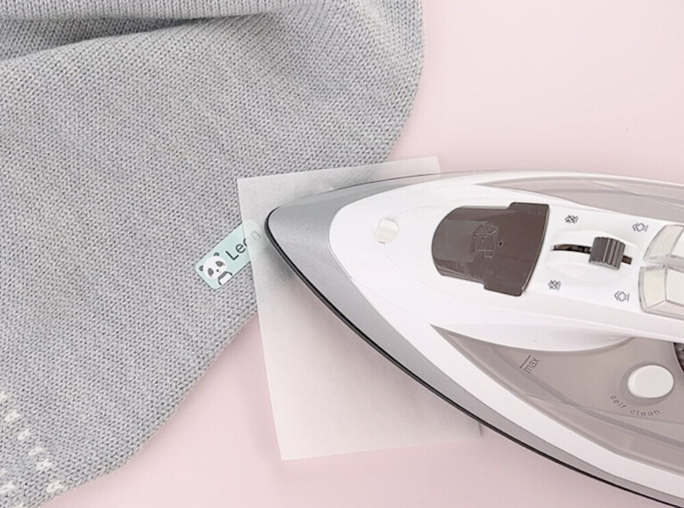 Bügeletikett wird mit einem Bügeleisen auf einem Kleidungsstück befestigt