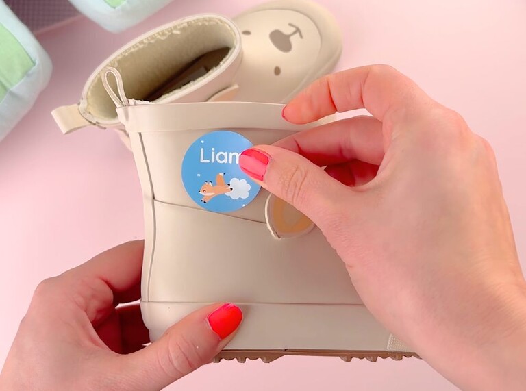 Blauer, runder Namensaufkleber mit einem kleinen Fuchs wird auf einen Gummistiefel geklebt.