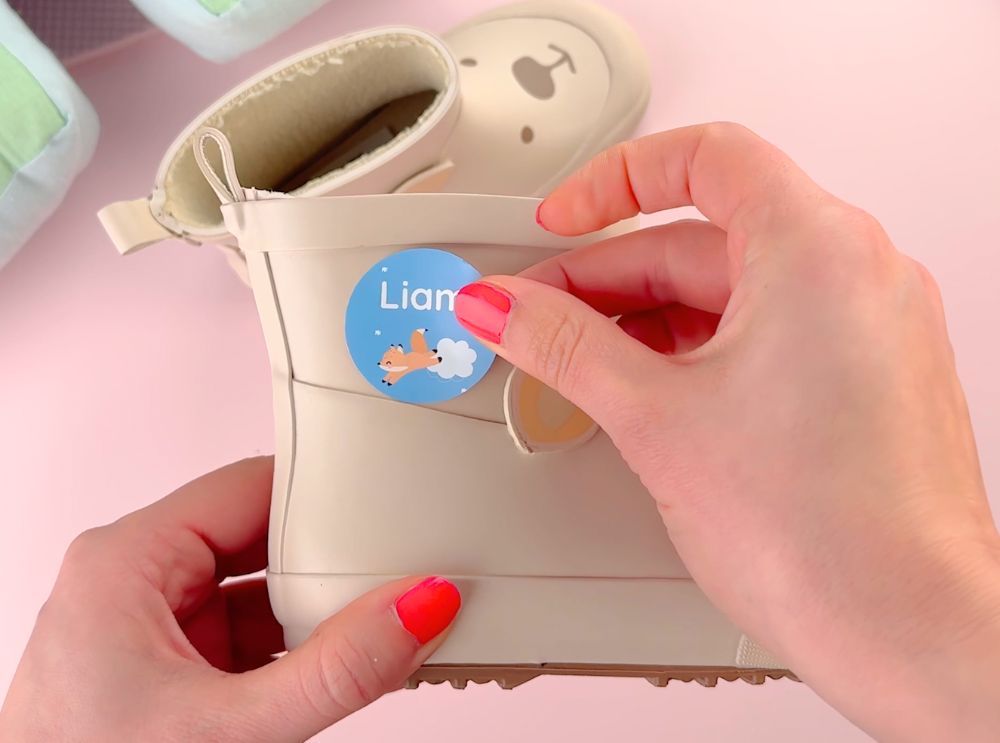 Blauer, runder Namensaufkleber mit einem kleinen Fuchs wird auf einen Gummistiefel geklebt.