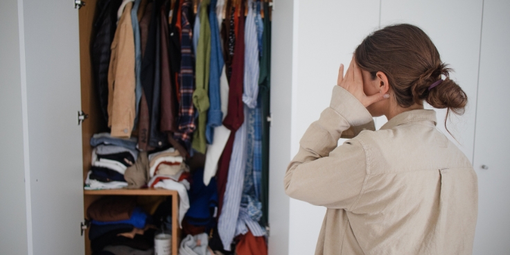 Frau mit Dutt steht vor offenem Kleiderschrank, organisiert Kleidung