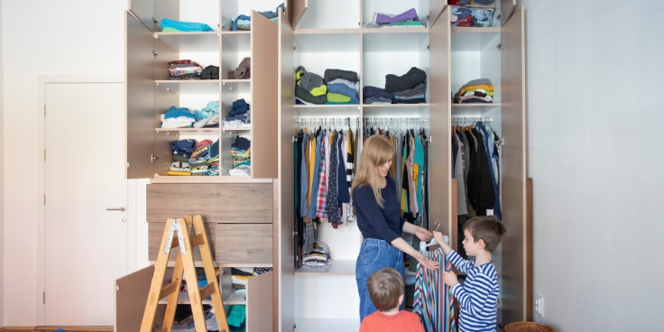 Mutter und kinder organisieren gemeinsam einen kleiderschrank, winterkleidung wird sortiert.