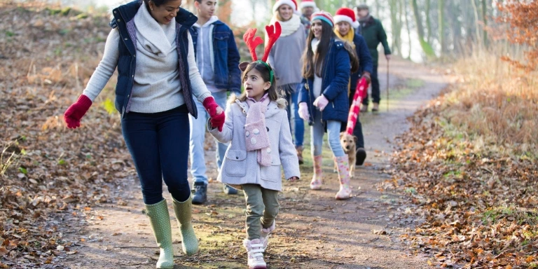 Gesund und organisiert durch den winter: tipps für familien 3 Familie unternimmt einen winterlichen spaziergang im wald, kinder tragen weihnachtliche accessoires.