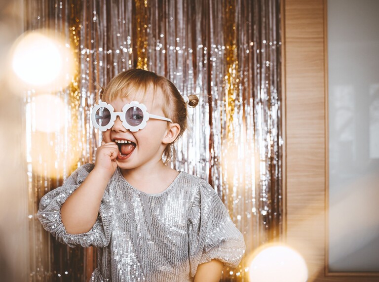 Lachendes Kind mit runder Sonnenbrille und Glitzervorhang