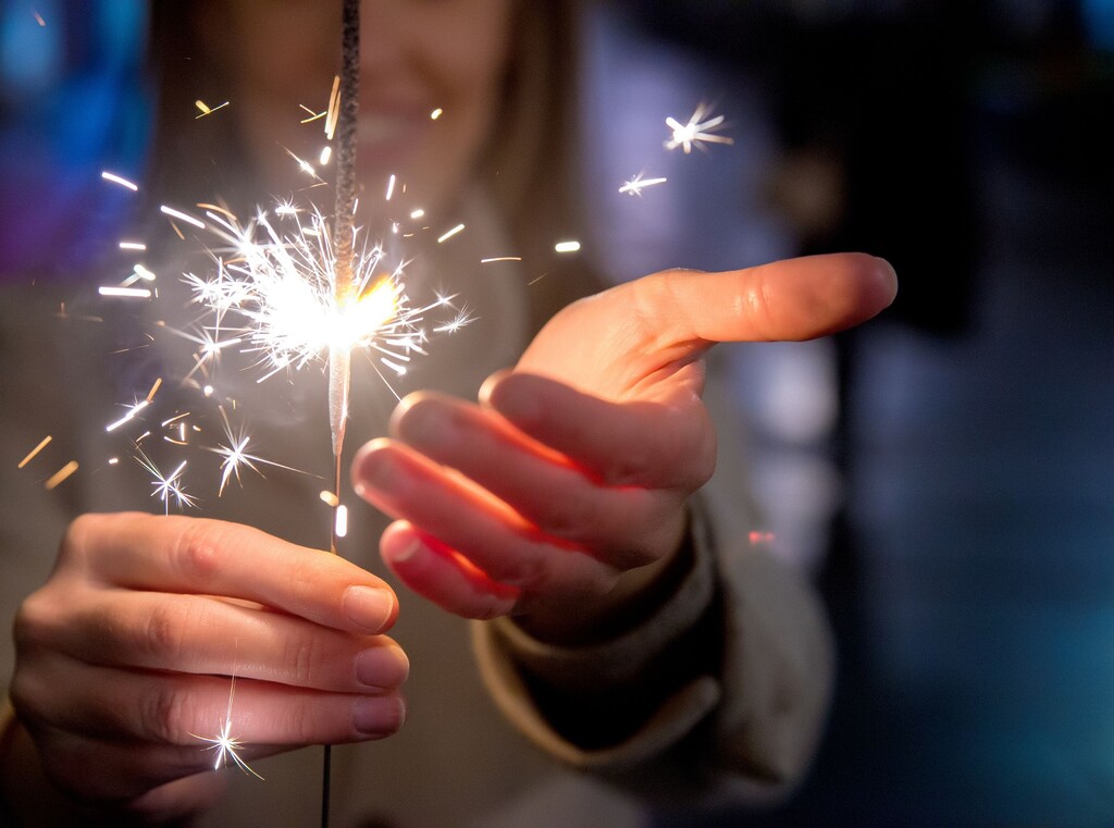 Hand hält brennende wunderkerze mit funkenflug, perfekt für silvesterstimmung
