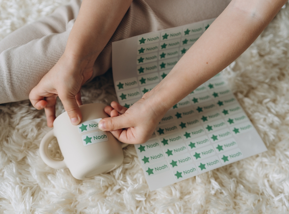Ein kind klebt namensaufkleber mit dem namen noah und einem grünen stern auf eine tasse