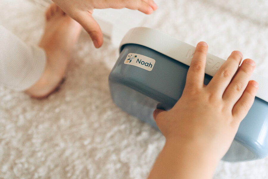Kinderhand mit blauer brotdose und personalisiertem sticker mit 'noah' und raketenmotiv.