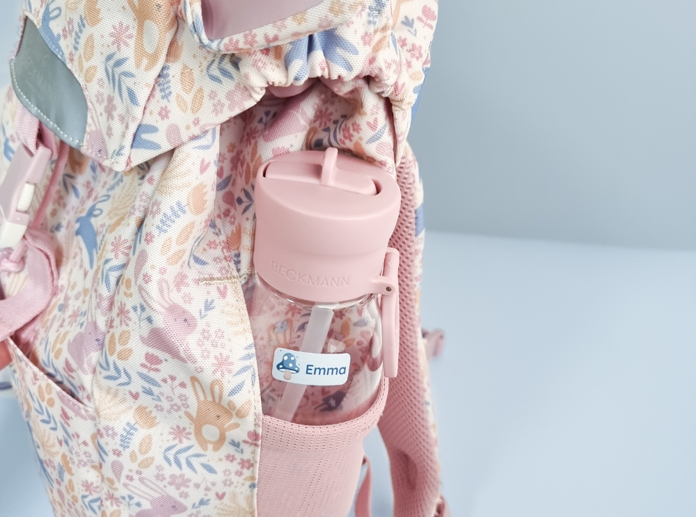 Wie du den perfekten schulranzen für dein kind auswählst 1 Nahaufnahme einer rosa trinkflasche mit namensaufkleber in der seitentasche eines geblümten rucksacks