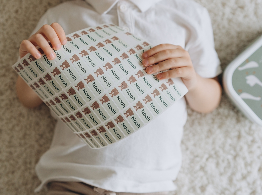 Kind hält einen bogen mit personalisierten namensaufklebern mit bärenmotiv und dem namen noah