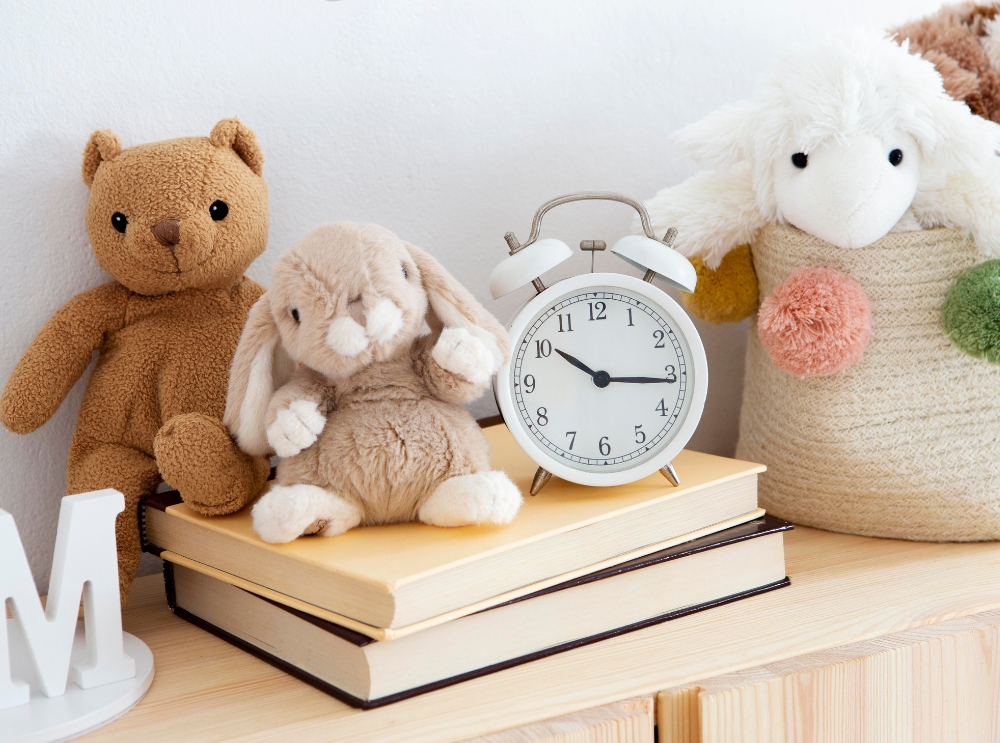 Stofftiere und ein weißer wecker auf einem stapel bücher in einer gemütlichen kinderzimmerecke