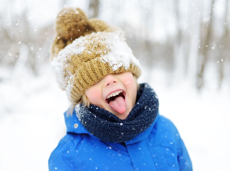 Child in winter clothes sticking out their tongue while snow falls.