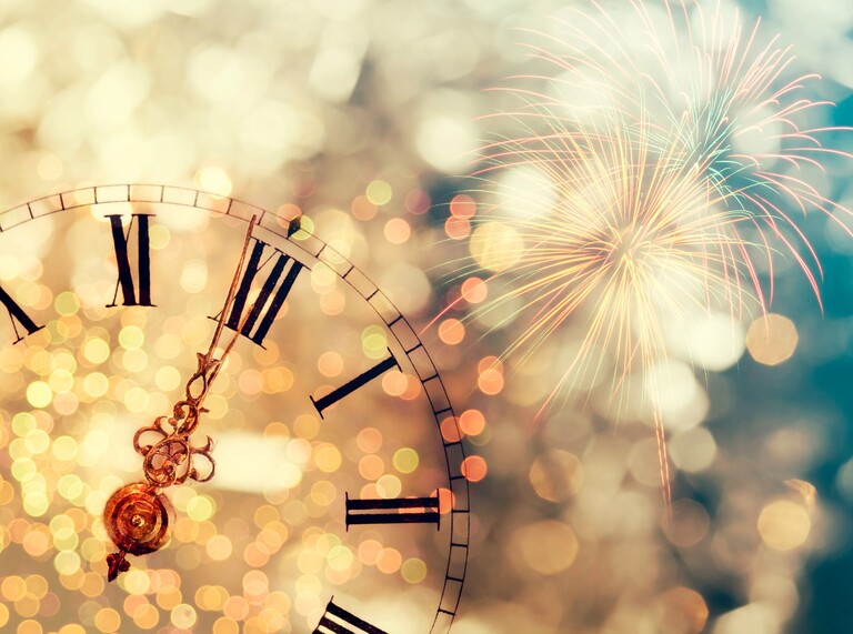 Vintage clock close to midnight with fireworks in the background.