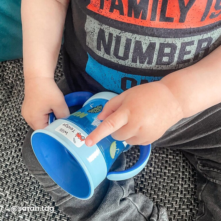 Kind klebt Namensaufkleber auf Trinkflasche