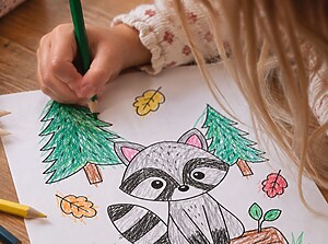 Ein Kind beugt sich über ein Ausmalbild mit Waldtieren und malt das Bild mit einem Buntstift aus